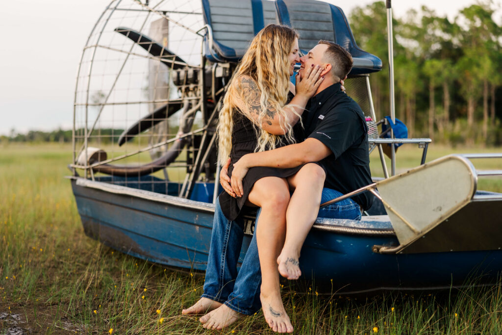 Cinematic, Central Florida engagement session shot out on an airboat in the Florida swamps. Man holds fiancé in his lap while they rub noses