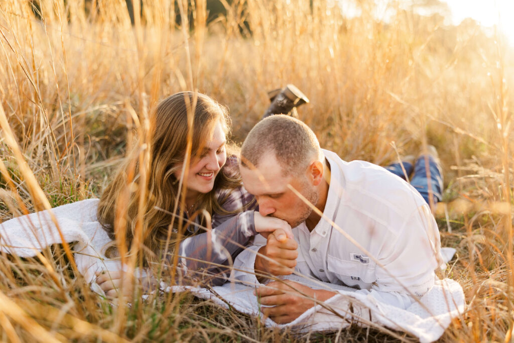 Emotive engaged couple lays in the tall amber Florida grasses, Man grabs and kisses his fiance's hand