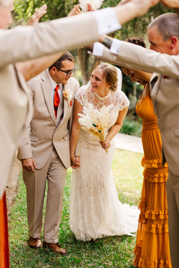 Just married FL couple smiles and laughs while walking through a tunnel created by the wedding party 